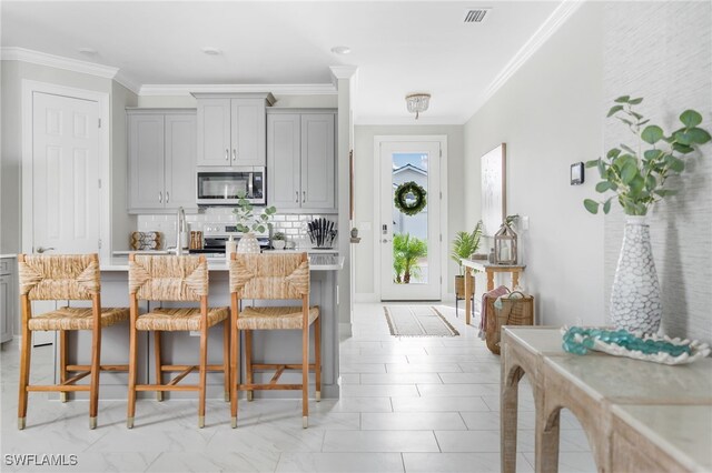 kitchen featuring tasteful backsplash, appliances with stainless steel finishes, a kitchen breakfast bar, gray cabinets, and ornamental molding