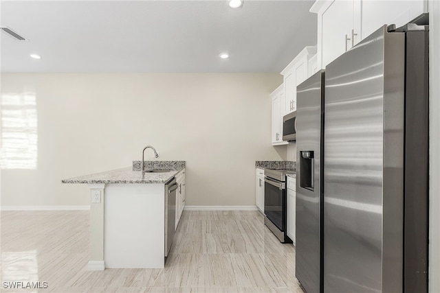 kitchen featuring kitchen peninsula, appliances with stainless steel finishes, white cabinetry, light stone countertops, and sink