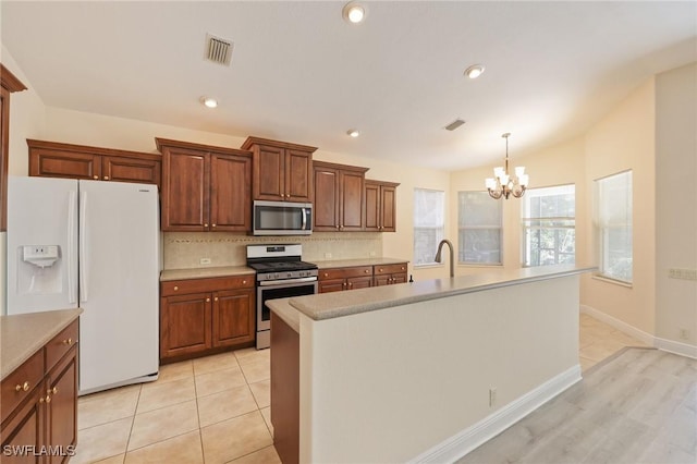 kitchen with decorative light fixtures, decorative backsplash, an island with sink, appliances with stainless steel finishes, and a notable chandelier