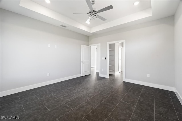 tiled empty room featuring a tray ceiling, built in features, and ceiling fan