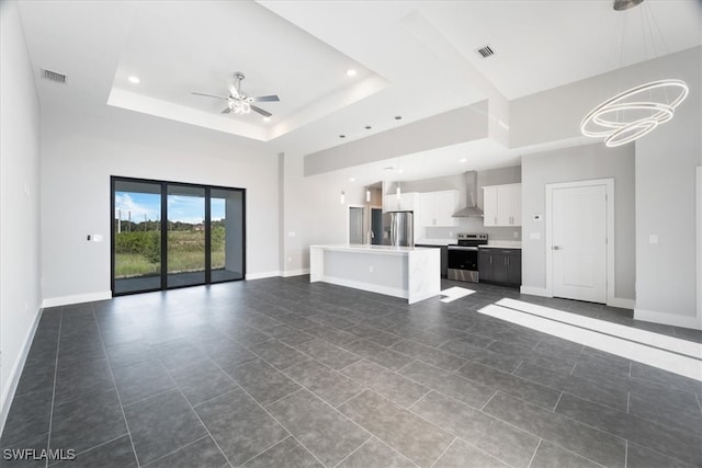 unfurnished living room with dark tile patterned floors, a tray ceiling, and ceiling fan with notable chandelier