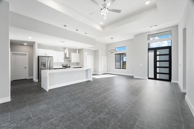 unfurnished living room featuring dark tile patterned floors, ceiling fan with notable chandelier, and a raised ceiling