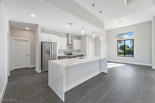 kitchen featuring appliances with stainless steel finishes, white cabinetry, a kitchen island with sink, wall chimney exhaust hood, and decorative light fixtures