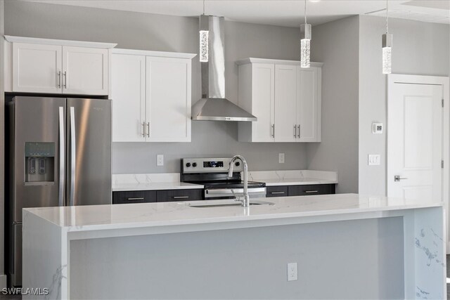 kitchen featuring a center island with sink, appliances with stainless steel finishes, white cabinetry, wall chimney exhaust hood, and decorative light fixtures