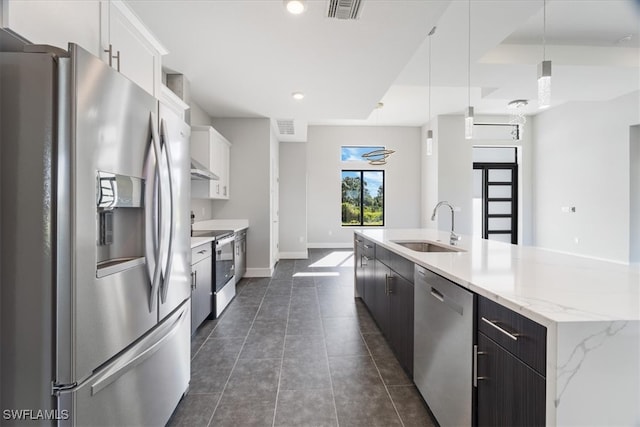 kitchen with appliances with stainless steel finishes, sink, dark tile patterned floors, pendant lighting, and white cabinets