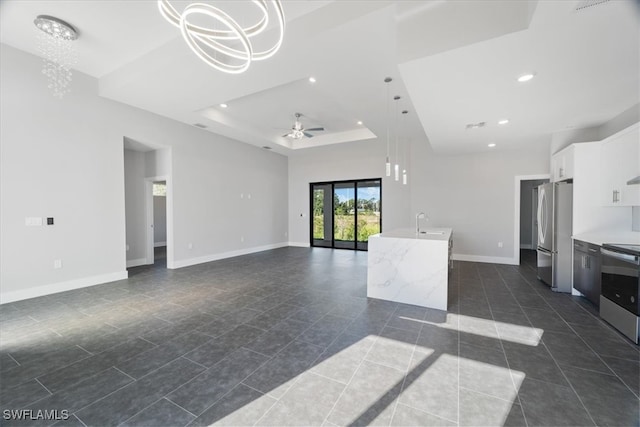 unfurnished living room with sink, a raised ceiling, ceiling fan with notable chandelier, and dark tile patterned flooring