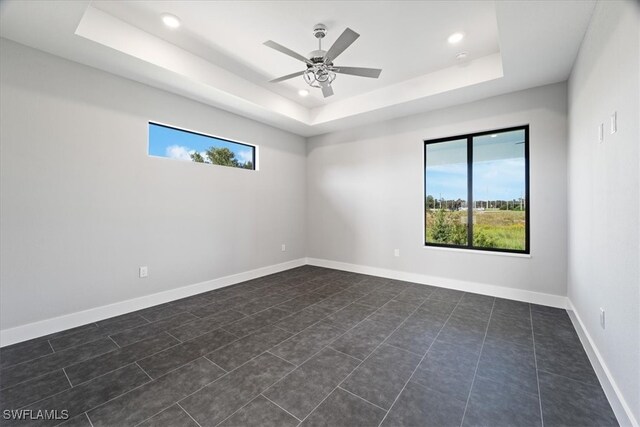 tiled empty room with ceiling fan, a raised ceiling, and plenty of natural light