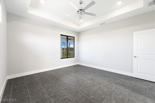 empty room with dark tile patterned flooring, a tray ceiling, and ceiling fan