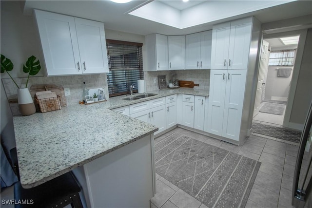 kitchen featuring white cabinetry, decorative backsplash, sink, kitchen peninsula, and light stone counters