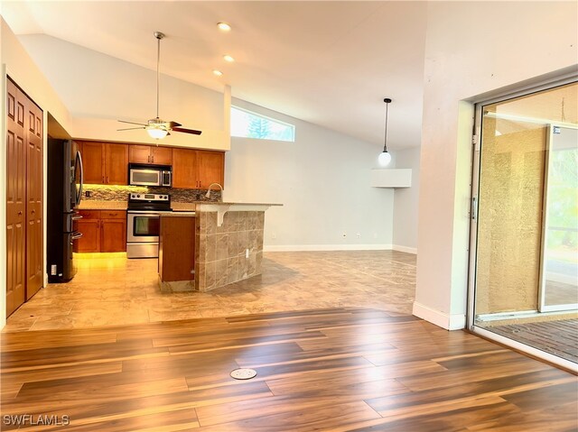 kitchen with light hardwood / wood-style floors, decorative light fixtures, stainless steel appliances, and high vaulted ceiling