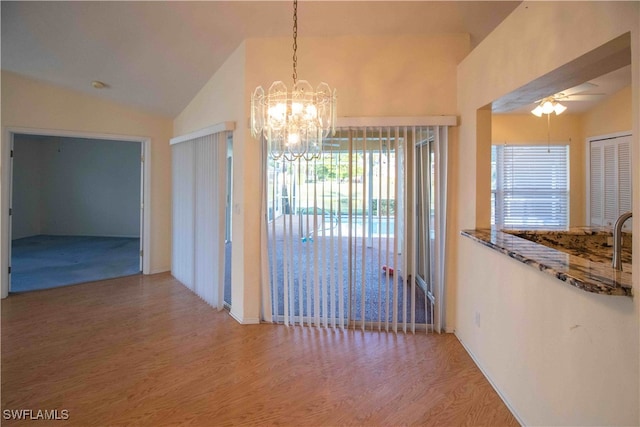 unfurnished dining area featuring hardwood / wood-style flooring, a healthy amount of sunlight, vaulted ceiling, and ceiling fan with notable chandelier