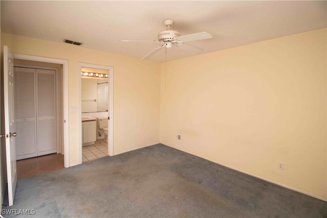 unfurnished bedroom featuring light carpet, a closet, ensuite bath, and ceiling fan