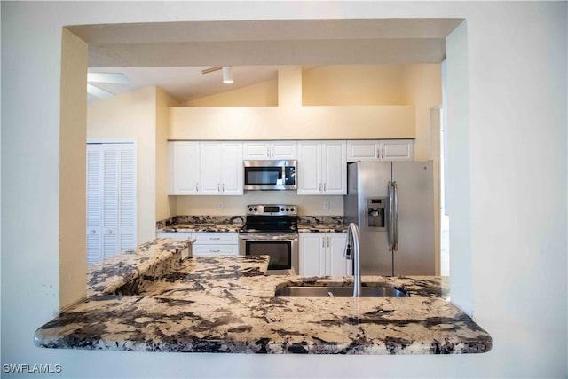 kitchen featuring white cabinets, appliances with stainless steel finishes, vaulted ceiling, dark stone countertops, and sink