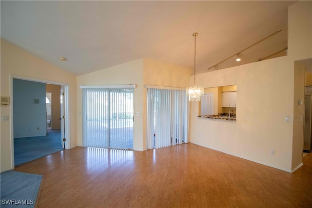 unfurnished living room featuring an inviting chandelier, rail lighting, wood-type flooring, and vaulted ceiling