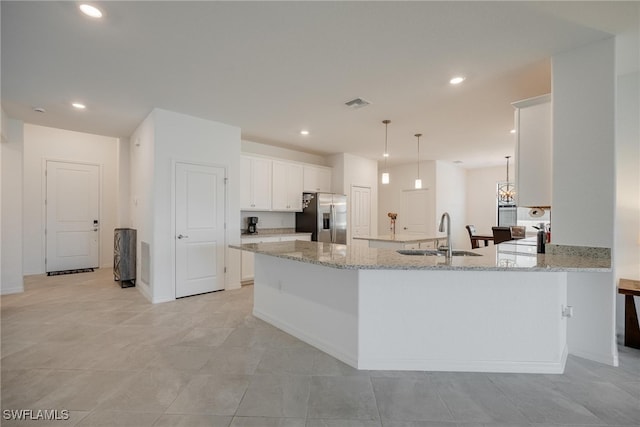 kitchen with sink, kitchen peninsula, stainless steel fridge, white cabinetry, and pendant lighting