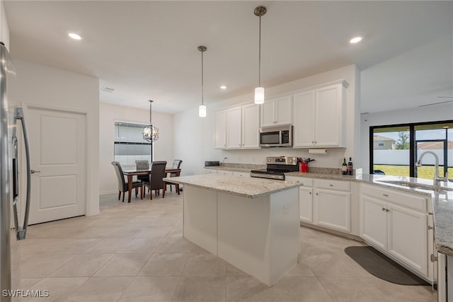 kitchen with light stone counters, white cabinetry, stainless steel appliances, sink, and a center island