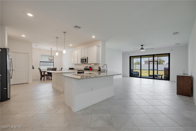 kitchen with kitchen peninsula, appliances with stainless steel finishes, white cabinetry, light stone countertops, and decorative light fixtures