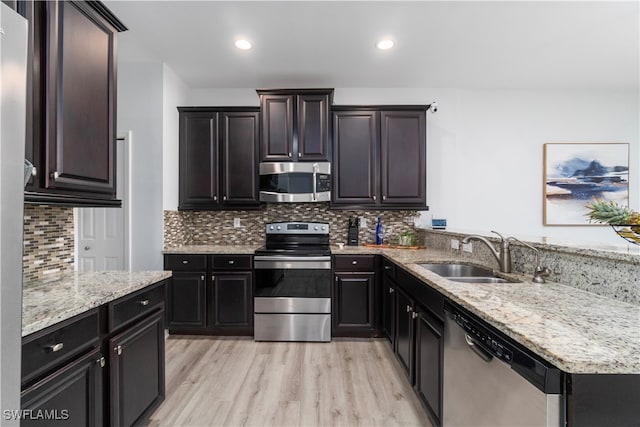 kitchen with light hardwood / wood-style floors, stainless steel appliances, light stone countertops, and sink