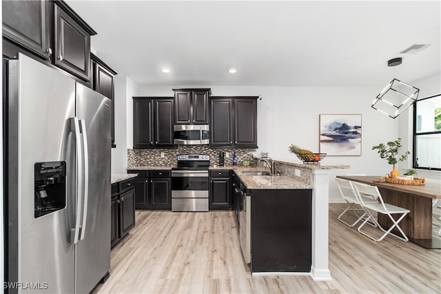 kitchen with light stone counters, light hardwood / wood-style flooring, stainless steel appliances, sink, and decorative light fixtures