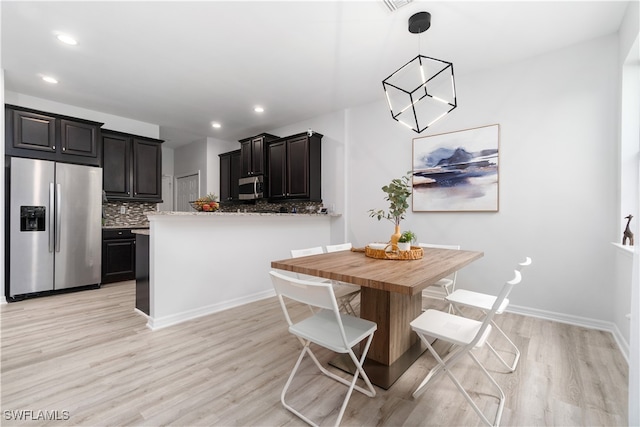 interior space with kitchen peninsula, decorative backsplash, hanging light fixtures, appliances with stainless steel finishes, and light hardwood / wood-style flooring