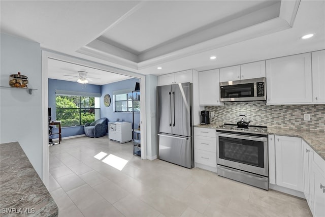 kitchen featuring decorative backsplash, white cabinets, a raised ceiling, ceiling fan, and stainless steel appliances