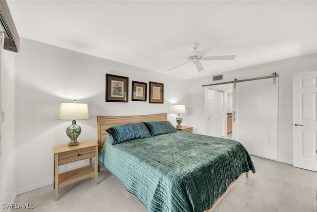 tiled bedroom featuring a barn door, ensuite bath, and ceiling fan