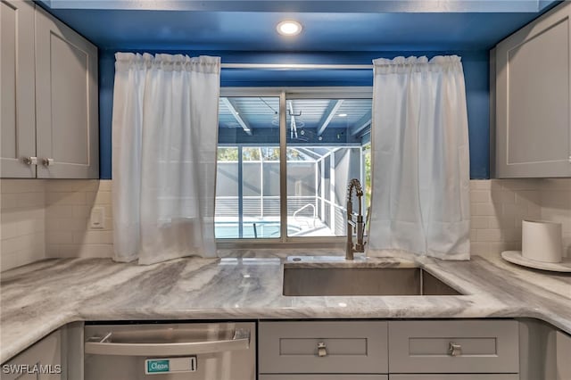 kitchen featuring gray cabinetry, dishwasher, sink, tasteful backsplash, and light stone counters