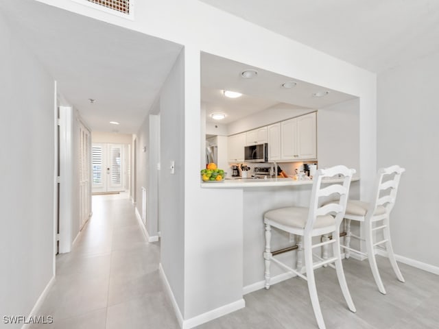 kitchen with a kitchen bar, white cabinetry, kitchen peninsula, and appliances with stainless steel finishes