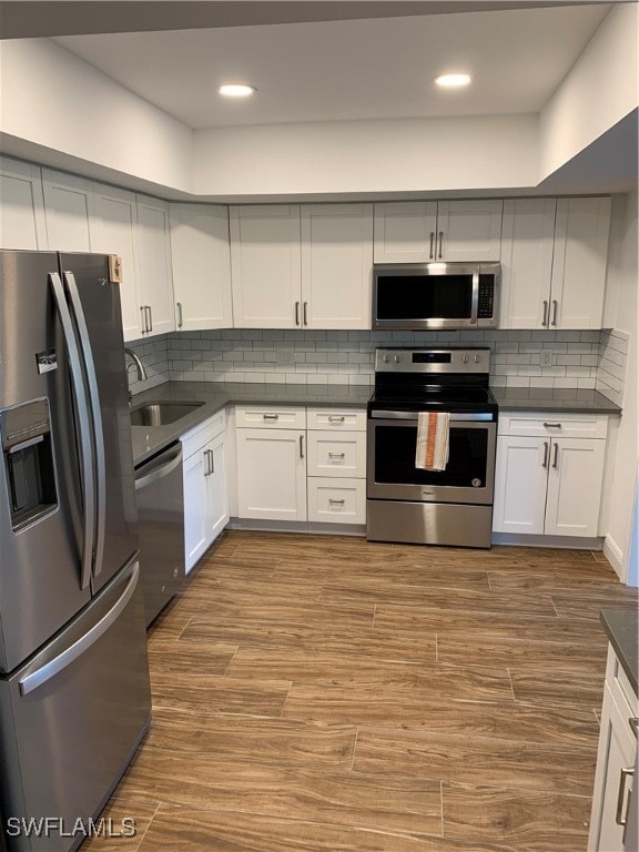 kitchen with hardwood / wood-style floors, white cabinets, decorative backsplash, and appliances with stainless steel finishes