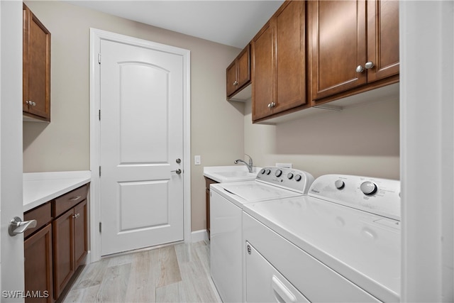 clothes washing area with washing machine and dryer, sink, light wood-type flooring, and cabinets