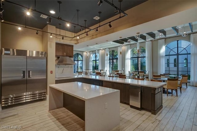 kitchen with a large island, light hardwood / wood-style flooring, a towering ceiling, high end fridge, and dark brown cabinetry