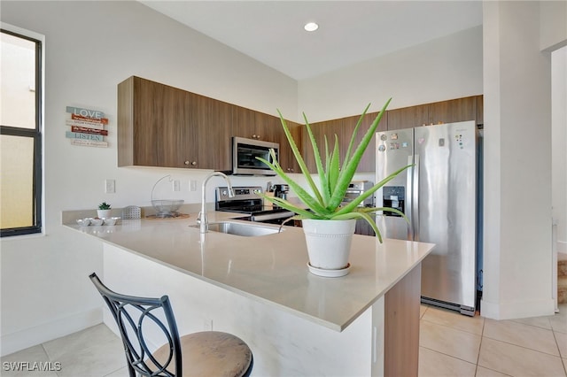 kitchen with a kitchen breakfast bar, kitchen peninsula, stainless steel appliances, sink, and light tile patterned flooring