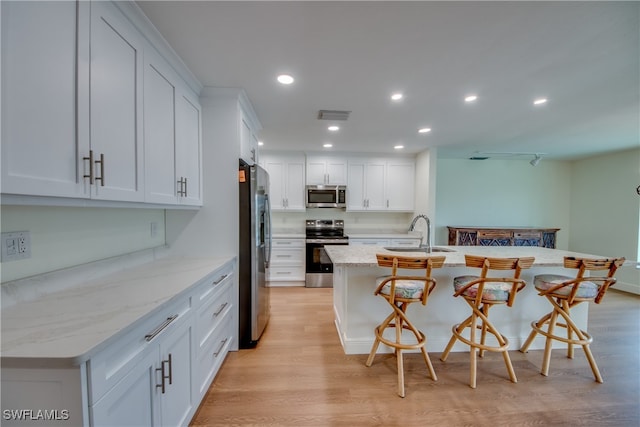 kitchen featuring appliances with stainless steel finishes, sink, white cabinets, a breakfast bar, and a kitchen island with sink