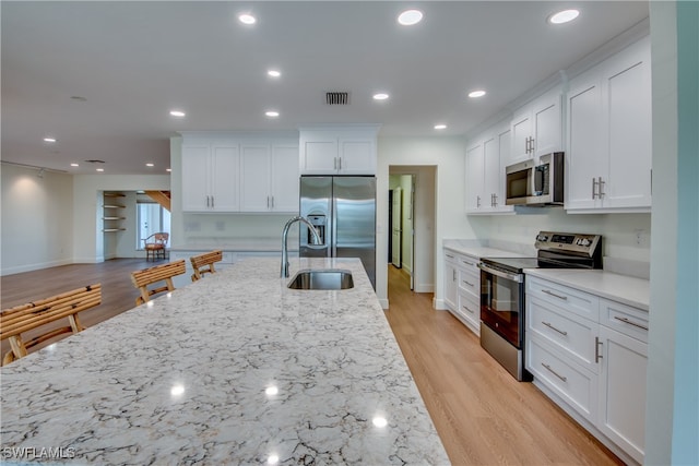 kitchen featuring stainless steel appliances, sink, light stone countertops, light wood-type flooring, and white cabinetry