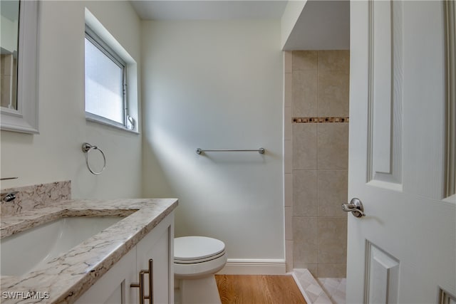 bathroom with toilet, vanity, wood-type flooring, and tiled shower