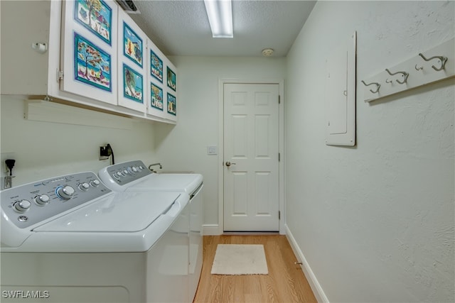 laundry room with light wood-type flooring, a textured ceiling, washing machine and clothes dryer, cabinets, and electric panel