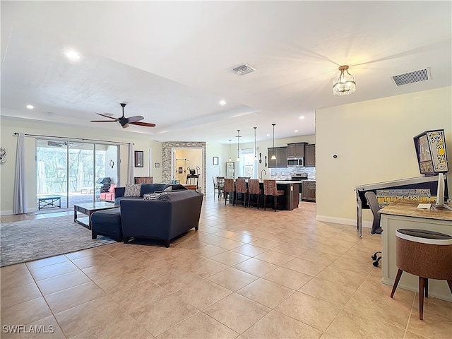 tiled living room featuring a tray ceiling and ceiling fan with notable chandelier