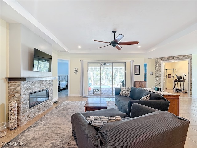 living room featuring ceiling fan, a raised ceiling, light tile patterned floors, and a fireplace