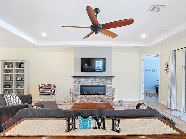 living room featuring ceiling fan, a tray ceiling, and a fireplace