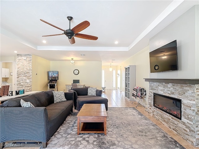 tiled living room with a fireplace, a tray ceiling, and ceiling fan