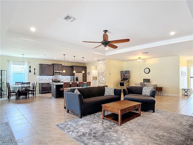 living room with ceiling fan, a raised ceiling, and light tile patterned floors