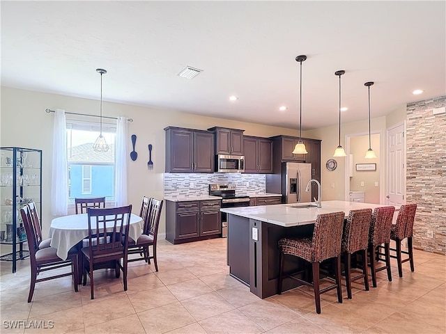 kitchen with a large island with sink, a kitchen breakfast bar, hanging light fixtures, backsplash, and appliances with stainless steel finishes