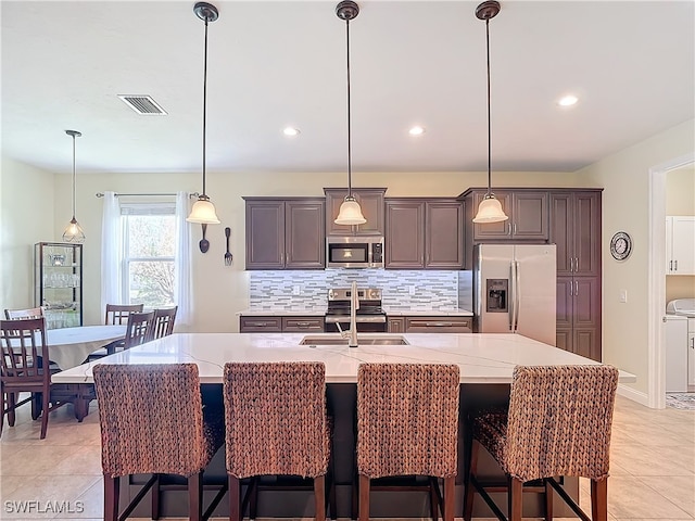 kitchen featuring a large island with sink, a breakfast bar area, hanging light fixtures, stainless steel appliances, and sink