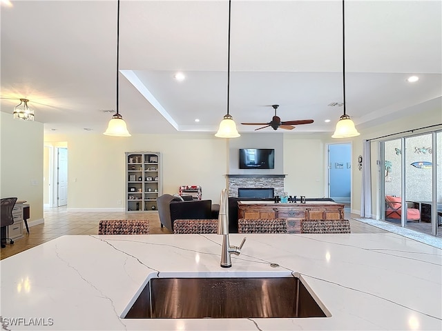 kitchen with ceiling fan, light stone countertops, a fireplace, pendant lighting, and sink