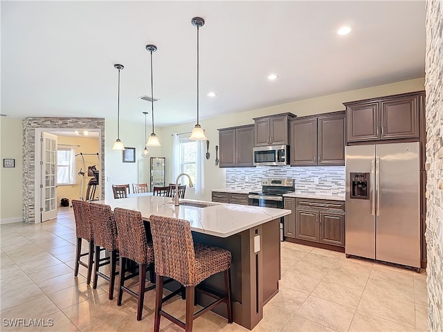 kitchen featuring sink, stainless steel appliances, decorative light fixtures, a breakfast bar area, and a kitchen island with sink