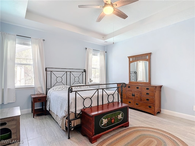 bedroom featuring ceiling fan, a raised ceiling, and light wood-type flooring