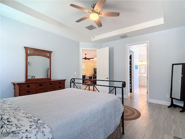 bedroom featuring light hardwood / wood-style floors, a walk in closet, a tray ceiling, and ceiling fan