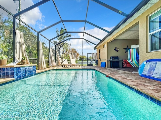 view of pool featuring a patio area, pool water feature, area for grilling, and glass enclosure