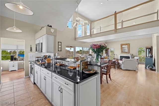 kitchen with backsplash, high vaulted ceiling, dark stone countertops, decorative light fixtures, and stainless steel appliances