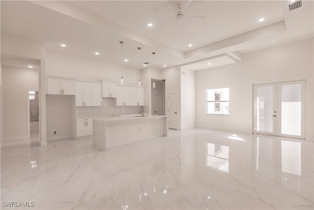 kitchen featuring a high ceiling, an island with sink, decorative light fixtures, white cabinetry, and ceiling fan